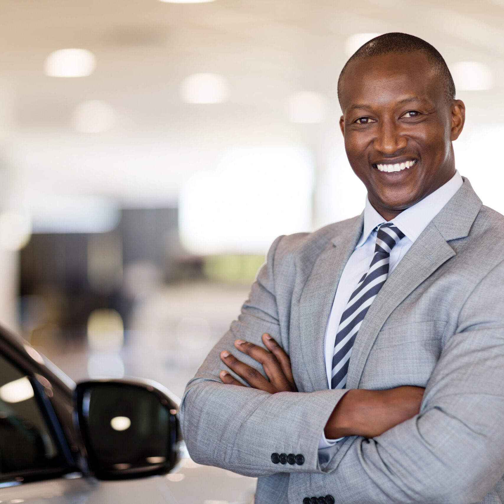 african american car dealership principal standing in vehicle showroom