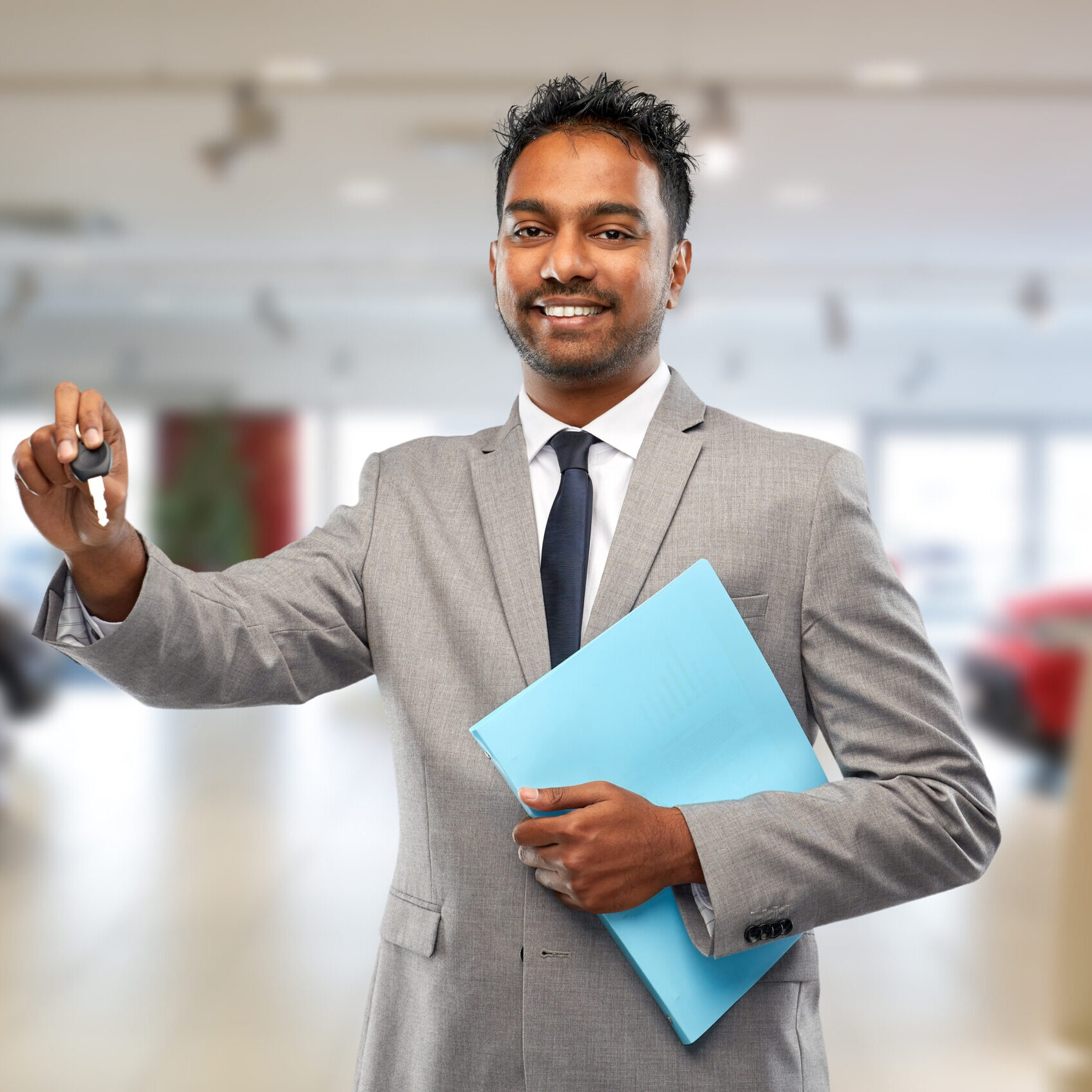 auto business, sale and people concept - happy indian car dealer showing key over showroom background